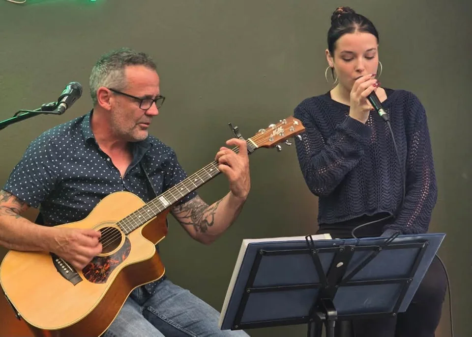 Dan playing acoustic guitar while Em sings into a microphone