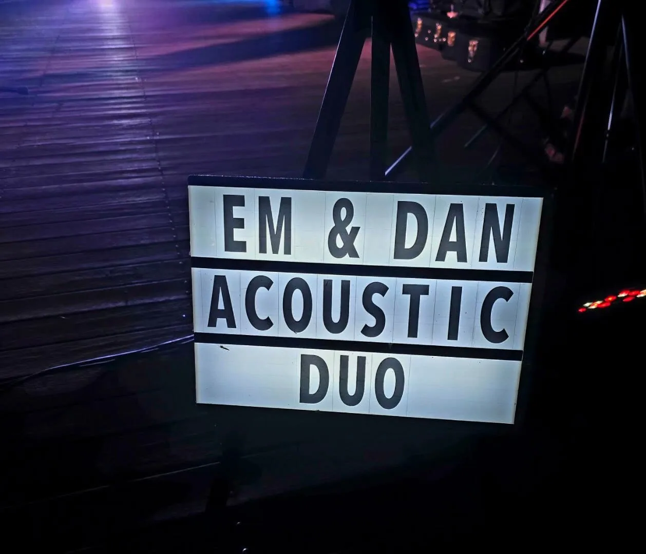 Lightbox sign reading “Em & Dan Acoustic Duo” at a night gig